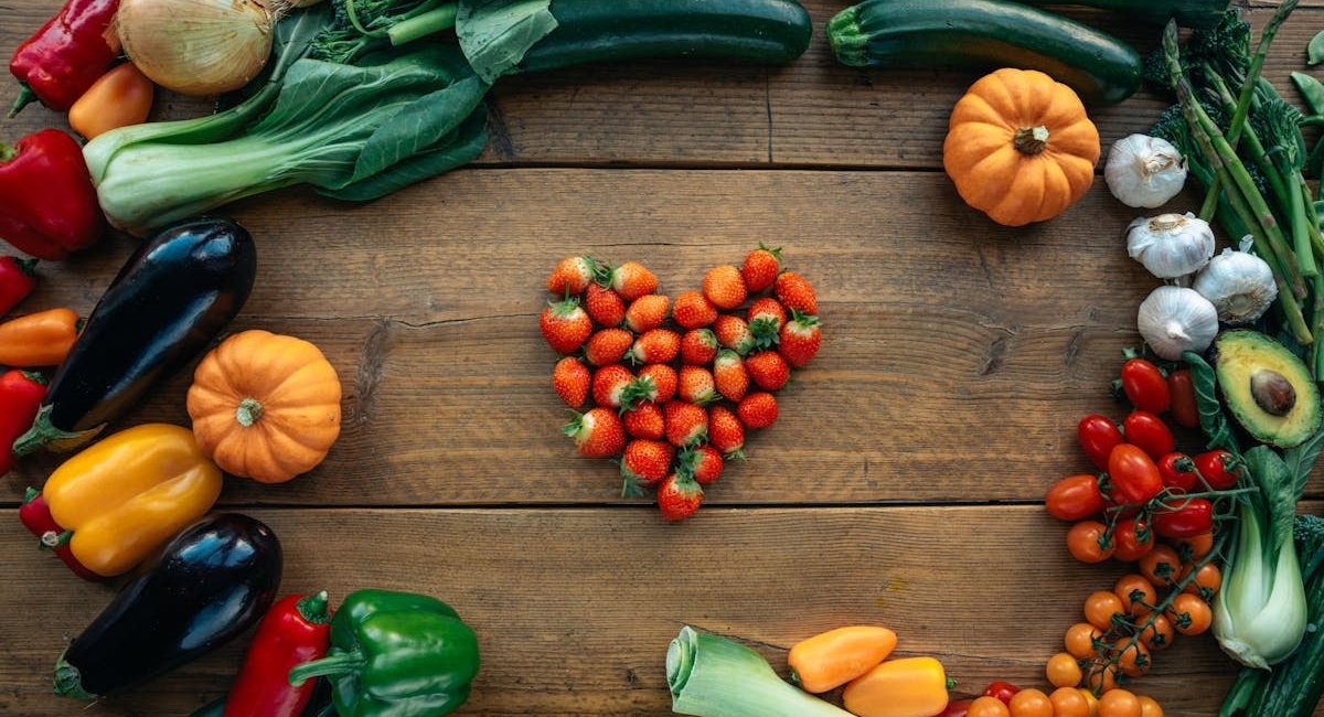 Vibrant fruits and vegetables arranged heart-shaped on a wooden surface, top view.