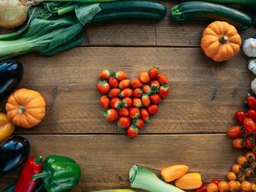 Vibrant fruits and vegetables arranged heart-shaped on a wooden surface, top view.