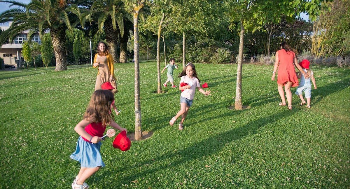 Kids and adults enjoy playing together in a lush, sunny park setting.