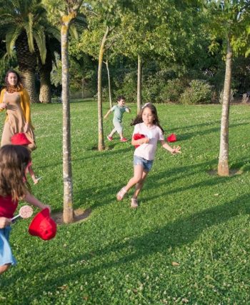 Kids and adults enjoy playing together in a lush, sunny park setting.