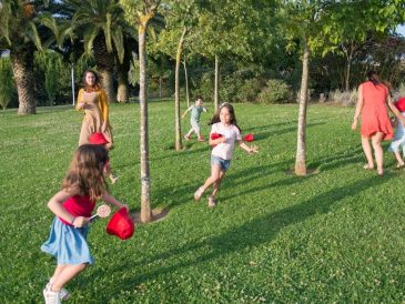 Kids and adults enjoy playing together in a lush, sunny park setting.