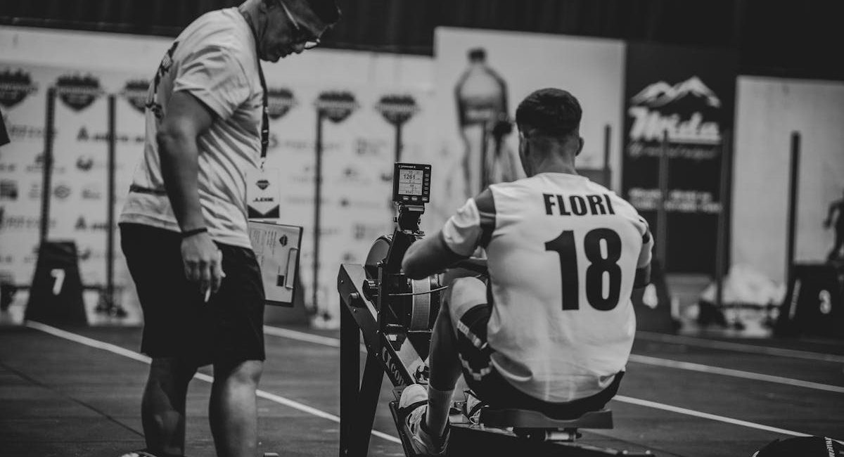 An athlete using a rowing machine indoors, coached in a gym setting.
