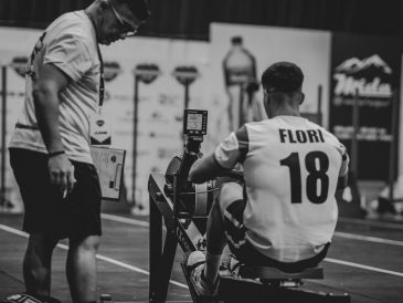 An athlete using a rowing machine indoors, coached in a gym setting.